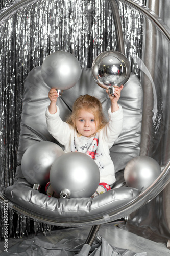 Little girl plays in a chair a glass bowl with silver balls. Snow queen cover