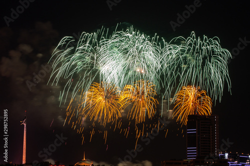 Beautiful colorful multicolor abstract firework or salute on the night black sky background, city with buildings on background. Celebration, New Year and anniversary concept