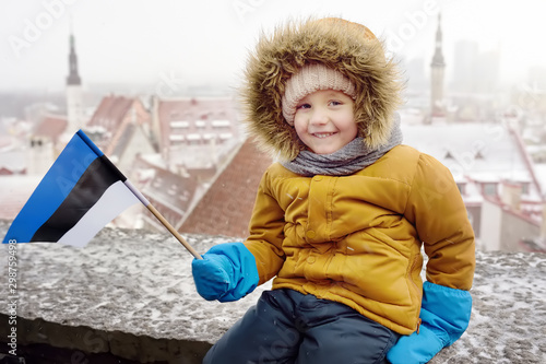 Foto Little boy with flag of Estonia is sitting on the wall of Tallinn old town in winter