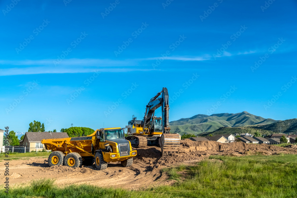Truck and excavator at a construction site with blue sky overhead on a sunny day Truck and excavator at a construction site with blue sky overhead on a sunny day