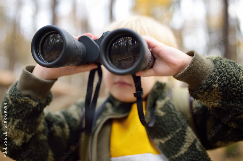 Little boy scout with binoculars during hiking in autumn forest. Child is looking through a binoculars. Little boy scout with binoculars during hiking in autumn forest. Child is looking through a binoculars.