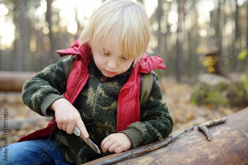Little boy scout is playing with knife in the forest. Child cuts with a knife on a log.