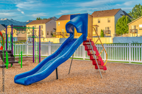 Blue slide with red stairs at a playground against homes mountain and blue sky photo