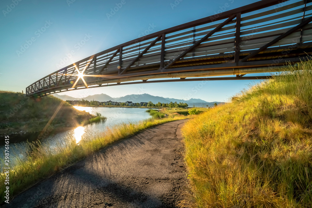 Fototapeta premium Trail along a lake and passing under a bridge with sun and blue sky overhead