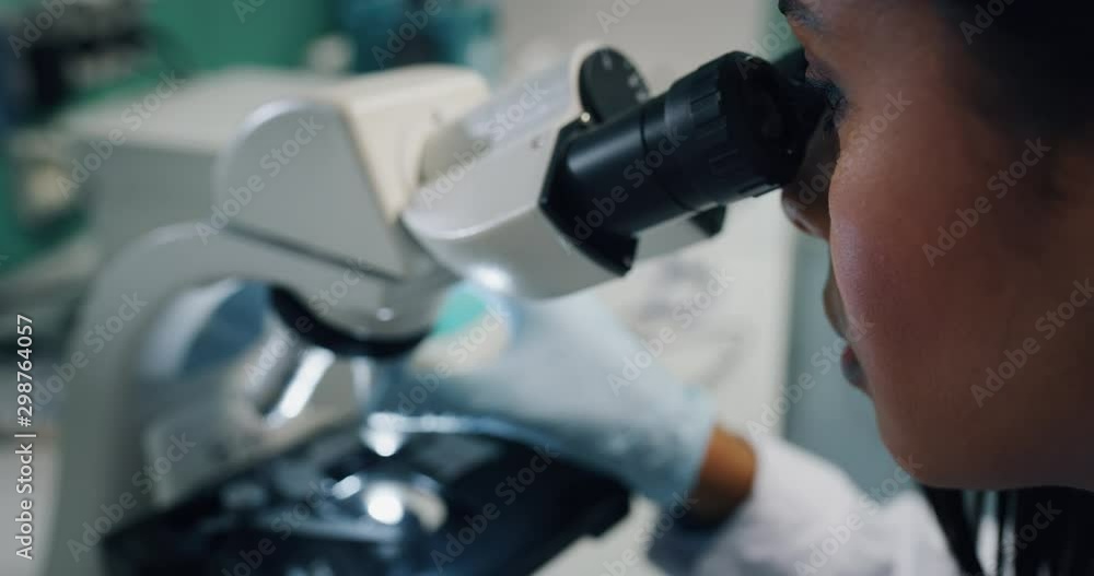 Close up of dark skin female scientist is analyzing a sample to extract the DNA and molecules with microscope in laboratory.