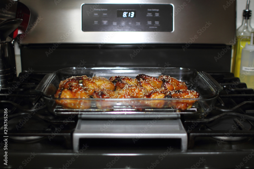 Baked teriayki chicken wings from the oven resting on the stove top in a home kitchen. Baked teriayki chicken wings from the oven resting on the stove top in a home kitchen.
