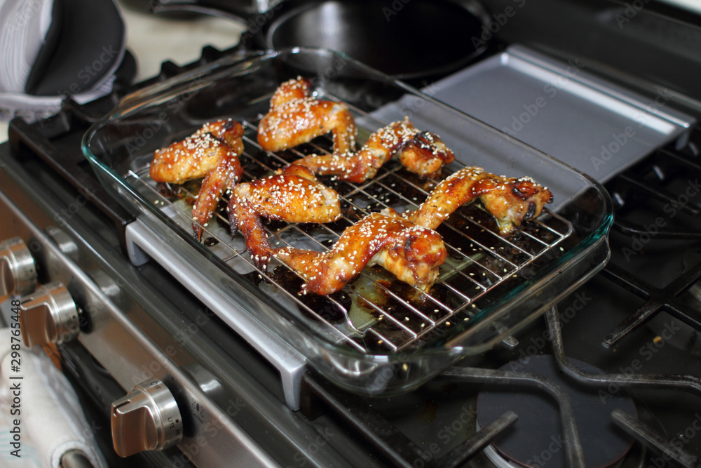 Baked teriayki chicken wings from the oven resting on the stove top in a home kitchen.