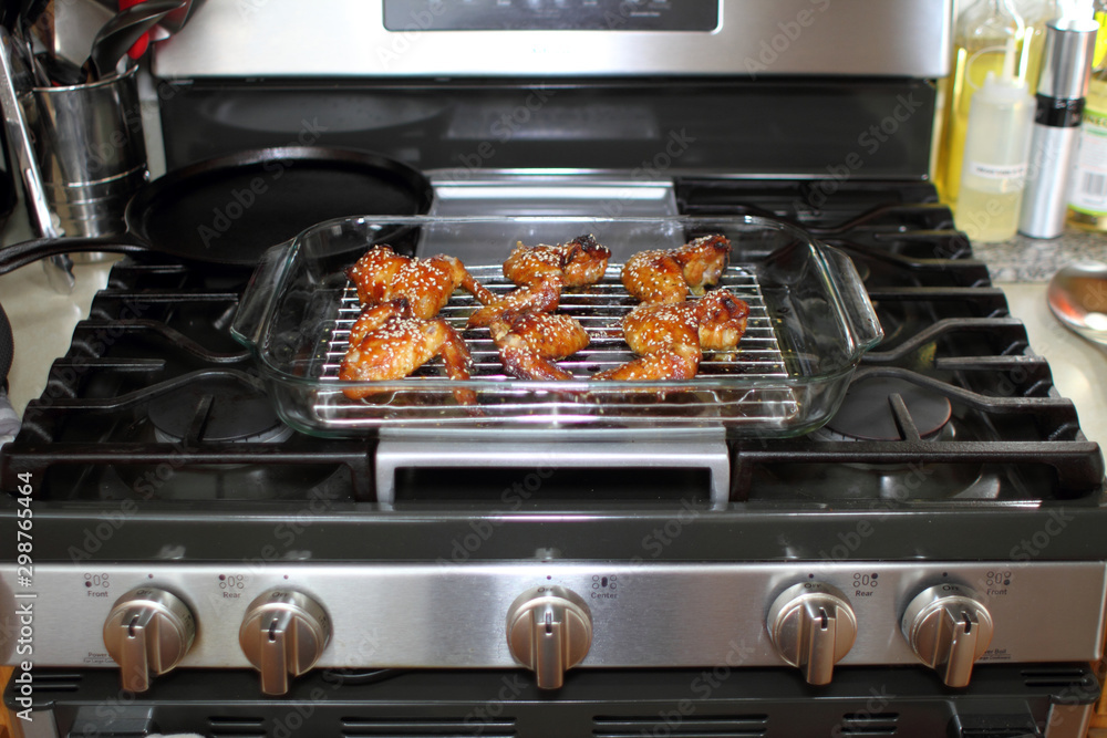 Baked teriayki chicken wings from the oven resting on the stove top in a home kitchen. Baked teriayki chicken wings from the oven resting on the stove top in a home kitchen.