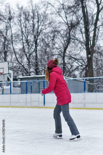 Beautiful girl having fun in winter park, balancing while skating at ice rink. Enjoying nature, winter time. Woman takes her first steps in figure skating