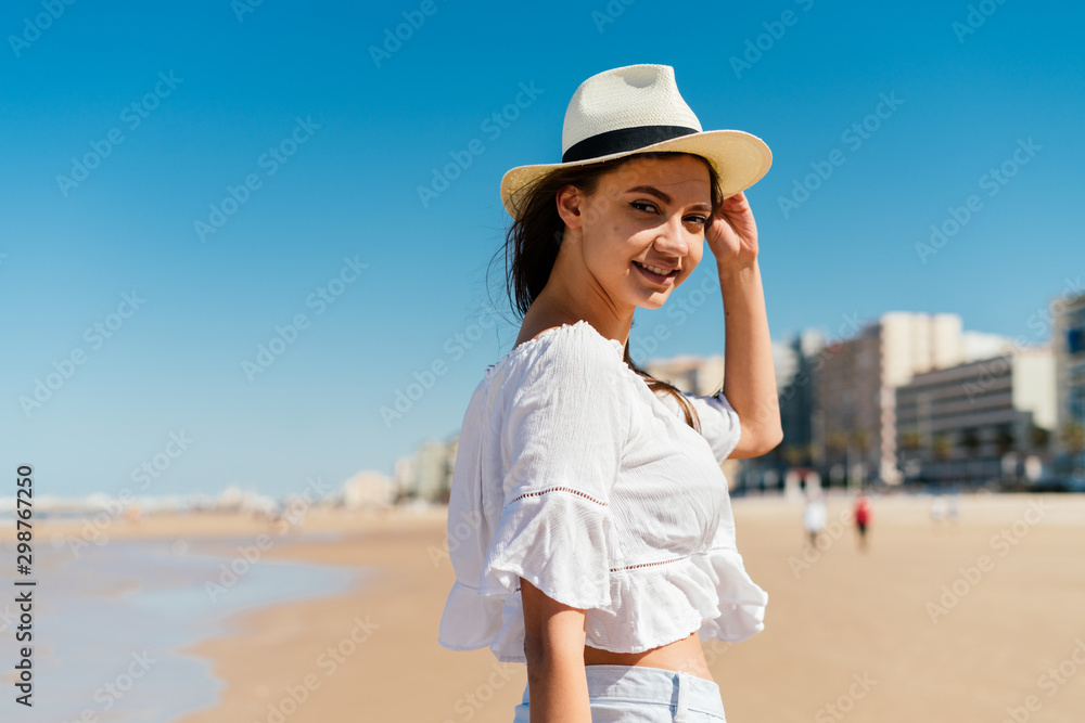 smiling girl in a hat and light clothes on the beach on the background of residential buildings