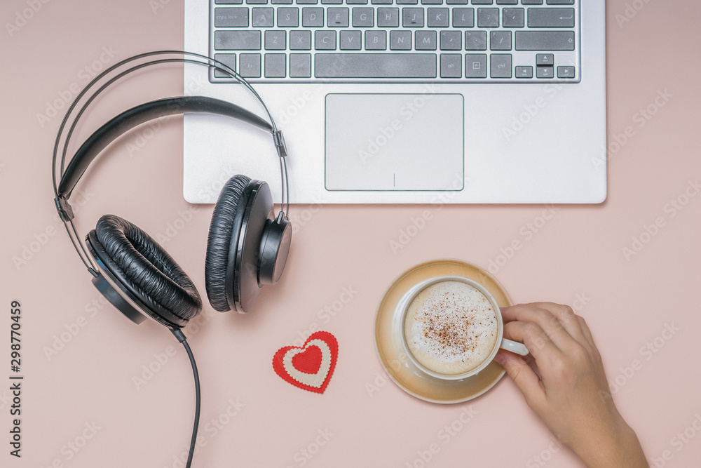Hand with a Cup of coffee, a laptop and headphones on a coral background. Job. Hand with a Cup of coffee, a laptop and headphones on a coral background. Job.
