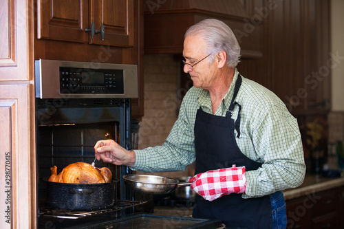 Good looking senior man basting a baking turkey