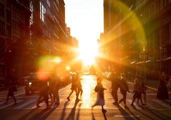 People walking across the street in New York City with the bright light of sunset shining between the buildings along 23rd St in Midtown Manhattan