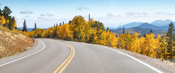 Empty road winds through a panoramic mountain landscape scene with golden fall aspen trees in the Colorado mountains