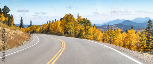 Empty road winds through a panoramic mountain landscape scene with golden fall aspen trees in the Colorado mountains photo