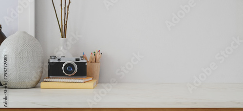 Minimal workspace with copy space, camera and office supplies on white desk and white wall photo