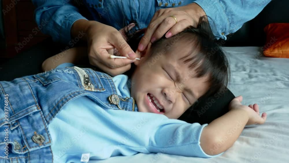 Asian mother using a cotton swab to clean the ears little child girl on the bed. Health care concept. Asian mother using a cotton swab to clean the ears little child girl on the bed. Health care concept.