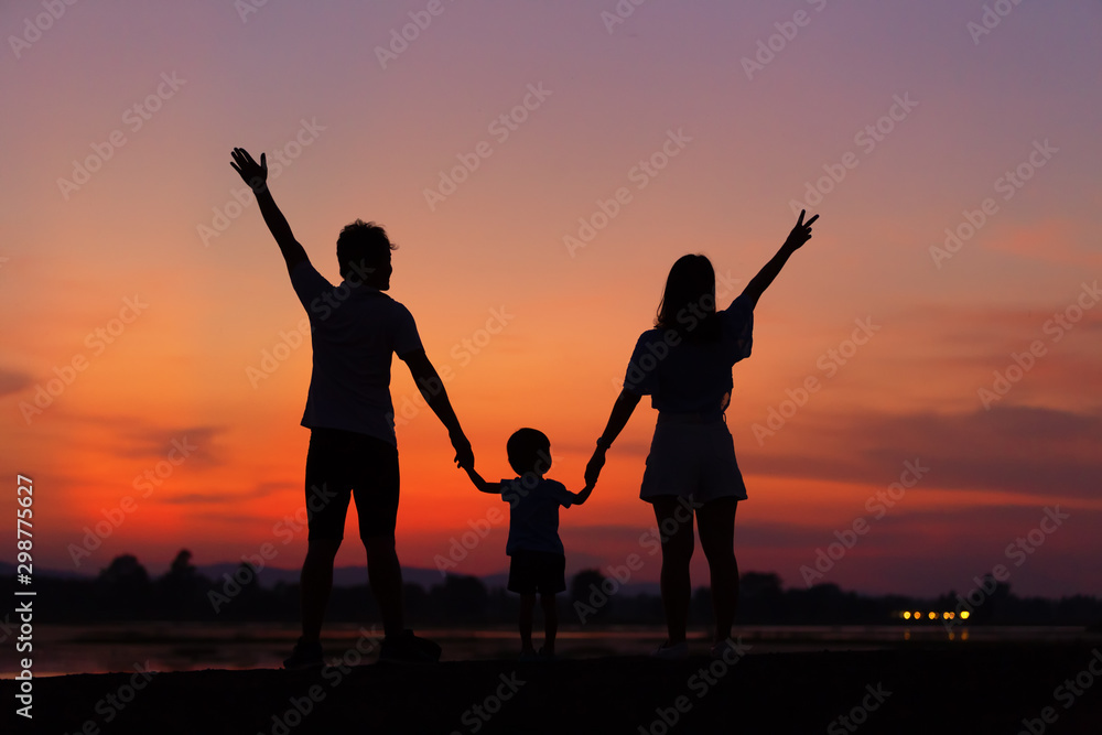 The silhouette of parents and children is enjoying the sunset in front of them consisting of father and mother and daughter.