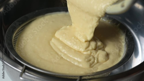 Pouring lumpy thick cream sauce into a strainer.