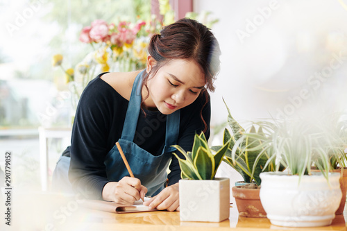 Young Asian florist writing down list of things she needs to do today