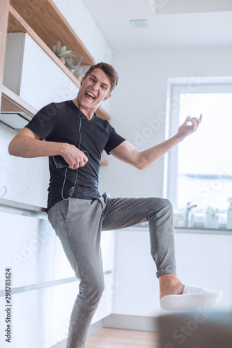 happy young man with smartphone sings in his kitchen