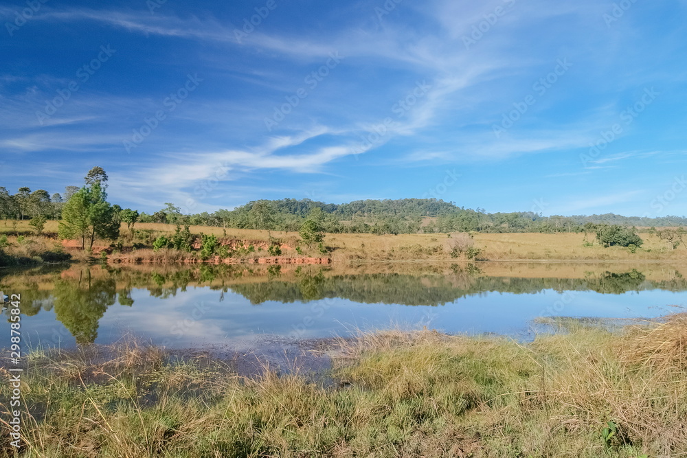 Swamp water on dry grass with reflection of the hill and cloudy in blue sky background, Thung Salang Luang, Phetchabun, Thailand.
