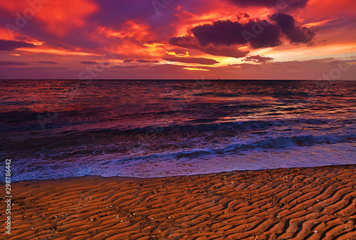 Beautiful vibrant dramatic cloudy sky winter sunset on a sandy textured beach.