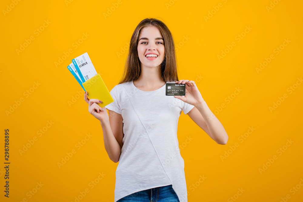 happy brunette woman with airplane tickets in passport and credit card isolated over yellow happy brunette woman with airplane tickets in passport and credit card isolated over yellow
