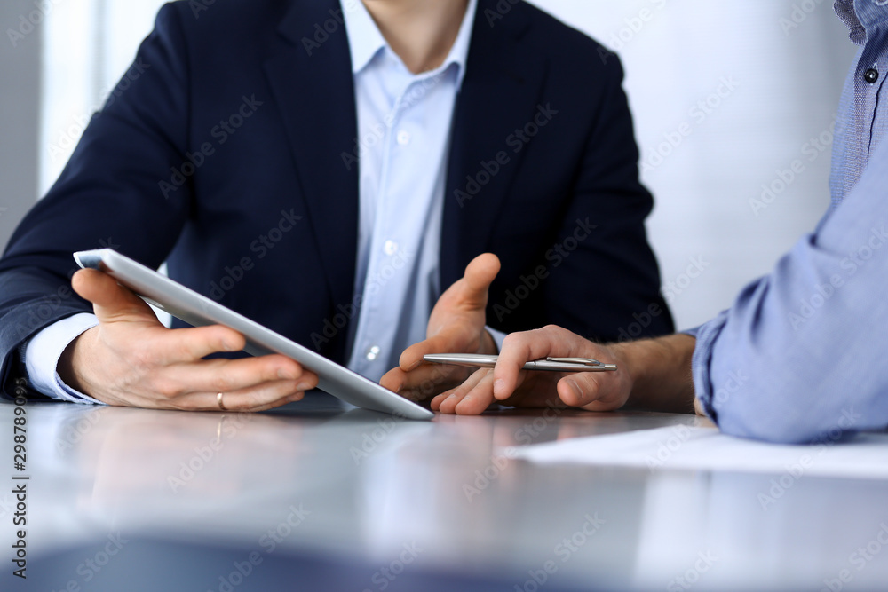 Business people using tablet computer while working together at the desk in modern office. Unknown businessman or male entrepreneur with colleague at workplace. Teamwork and partnership concept Business people using tablet computer while working together at the desk in modern office. Unknown businessman or male entrepreneur with colleague at workplace. Teamwork and partnership concept