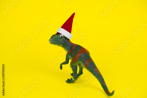 funny green dinosaur toy in little santa claus hat  on vibrant yellow background © dvulikaia