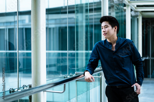 Portrait of smart businessman standing and  looking out through window at big city from an office building, think about Corporate vision, planning work, wait for meeting. © Ruttiyaphorn