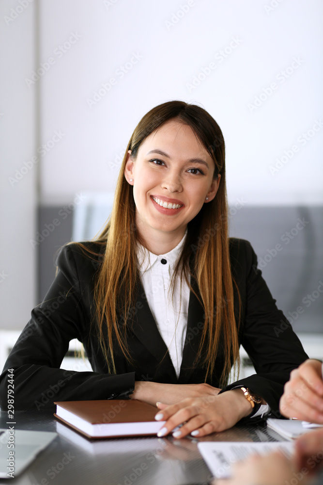 Happy smiling business woman headshot. Unknown businesswoman sitting at meeting or negotiation in modern office with colleagues at the background. Teamwork and partnership concept Happy smiling business woman headshot. Unknown businesswoman sitting at meeting or negotiation in modern office with colleagues at the background. Teamwork and partnership concept