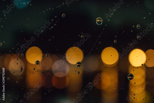 Fototapeta Naklejka Na Ścianę i Meble -  Blurred city lights with rain drops foreground. Unfocused colorful lights behind glass with drops. Shiny lights of night bokeh. Unfocused bright colors background.