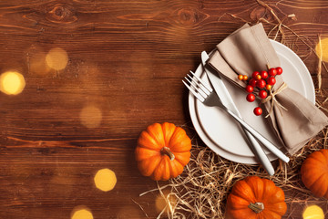 Place setting for Thanksgiving dinner with plate, napkin, cutlery and pumpkins on wooden table top view.