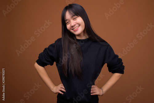 Young beautiful Asian woman wearing black sweater against brown © Ranta Images