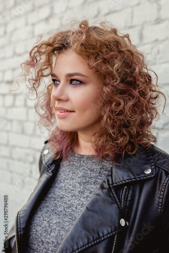 portrait of young beautiful cheerful woman with red curly hair on white bricks wall background. Film stylization