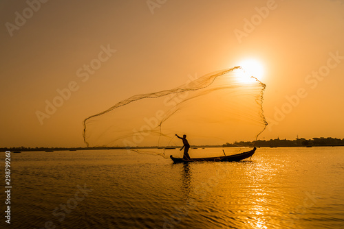 Silhouette Asian fisherman on wooden boat casting a net for freshwater fish at U Bein Bridge,Mandalay, Myanmar (Burma) in the early morning before sunrise 