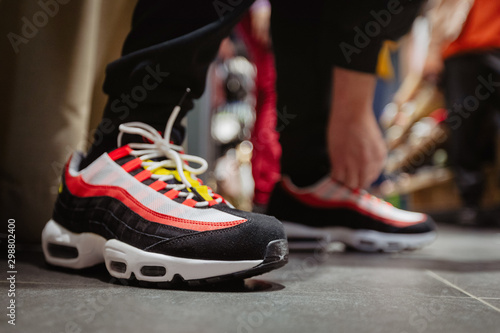 Side view of bright sneakers with black and red stripes on crop person bending to tie shoelaces on floor photo
