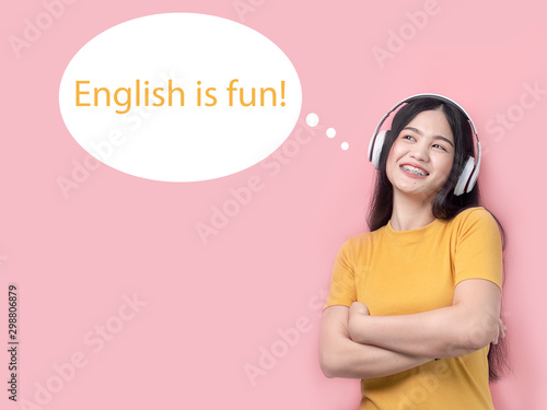 Happy Asian woman in yellow dress using headphone with pink background. English is fun message. photo