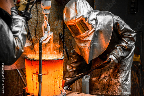 In a foundry workshop. Workers protected by their safety equipment handle a crucible containing molten metal