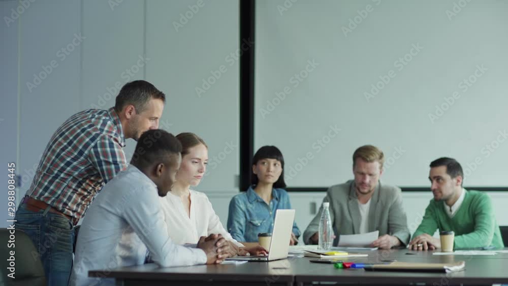 Tracking shot of diverse business people planning project in meeting room. Part of business team looking at presentation on laptop screen, their colleagues reading document Tracking shot of diverse business people planning project in meeting room. Part of business team looking at presentation on laptop screen, their colleagues reading document