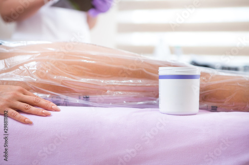 The process of anti-cellulite vacuum therapy with a bag is in progress  and next to the patient s leg is a box of cream used in the process.