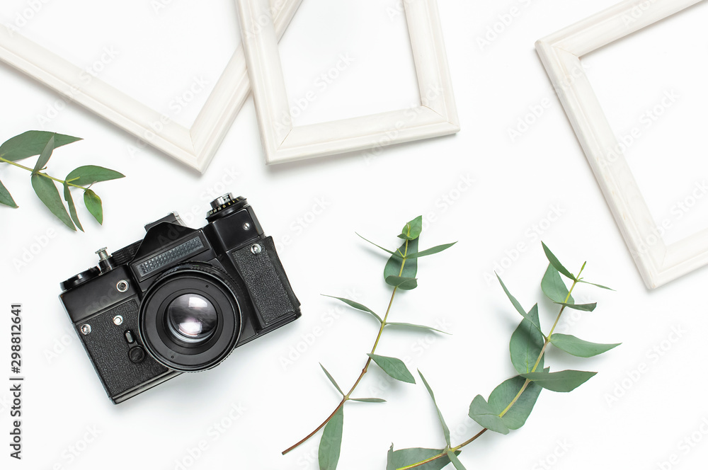 White photo frame, old retro photo camera and green eucalyptus leaves on white background. Flat lay top view copy space. Stylish minimal composition, artwork mockup, picture frame, home decoration - obrazy, fototapety, plakaty 
