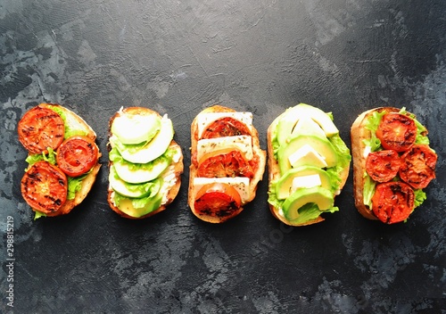 Bruschetta on a dark table background. Bruschetta with grilled  tomatoes, mozzarella and avocado. Delicious vegetarian healthy sandwiches. Tasty snack.