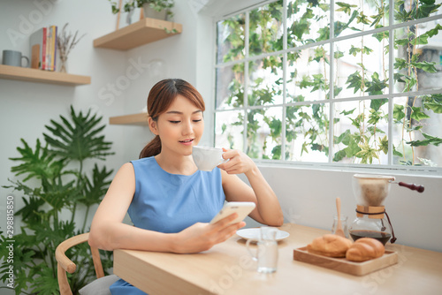 Beautiful Asian woman drinking coffee and using phone behind the window