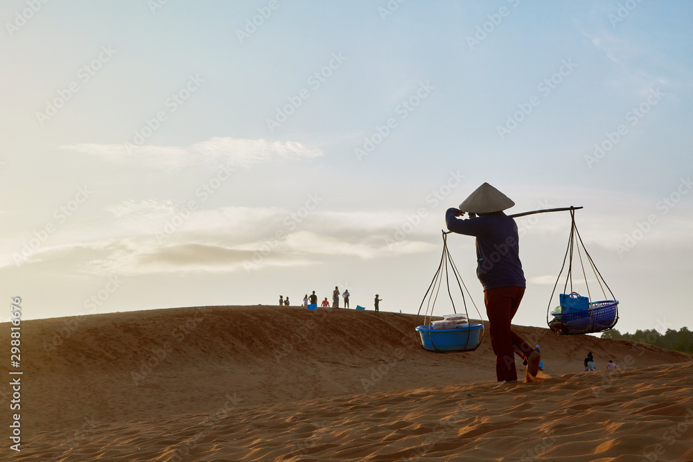 Fototapeta premium A man carries a load across the desert at sunset