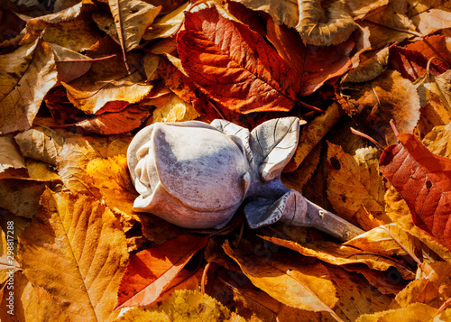 Eine Rose aus Stein zum Abschied im Herbstlaub.