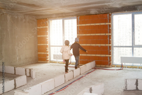 happy adorable little boy and girl go on foam blocks of first row of wall in huge space of new luxury modern apartment with panoramic windows in residential building under construction © sommersby
