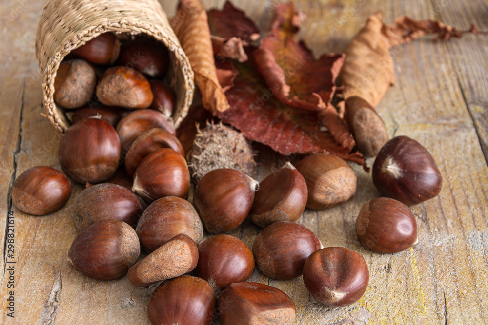 Top view of chestnuts with dried leaves and unfocused wrappers, on worn wooden background horizontally Top view of chestnuts with dried leaves and unfocused wrappers, on worn wooden background horizontally