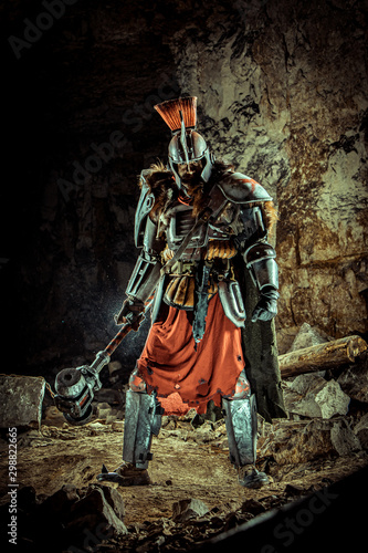 Powerful knight in the armor with the hammer. Dungeon on the background. © diter